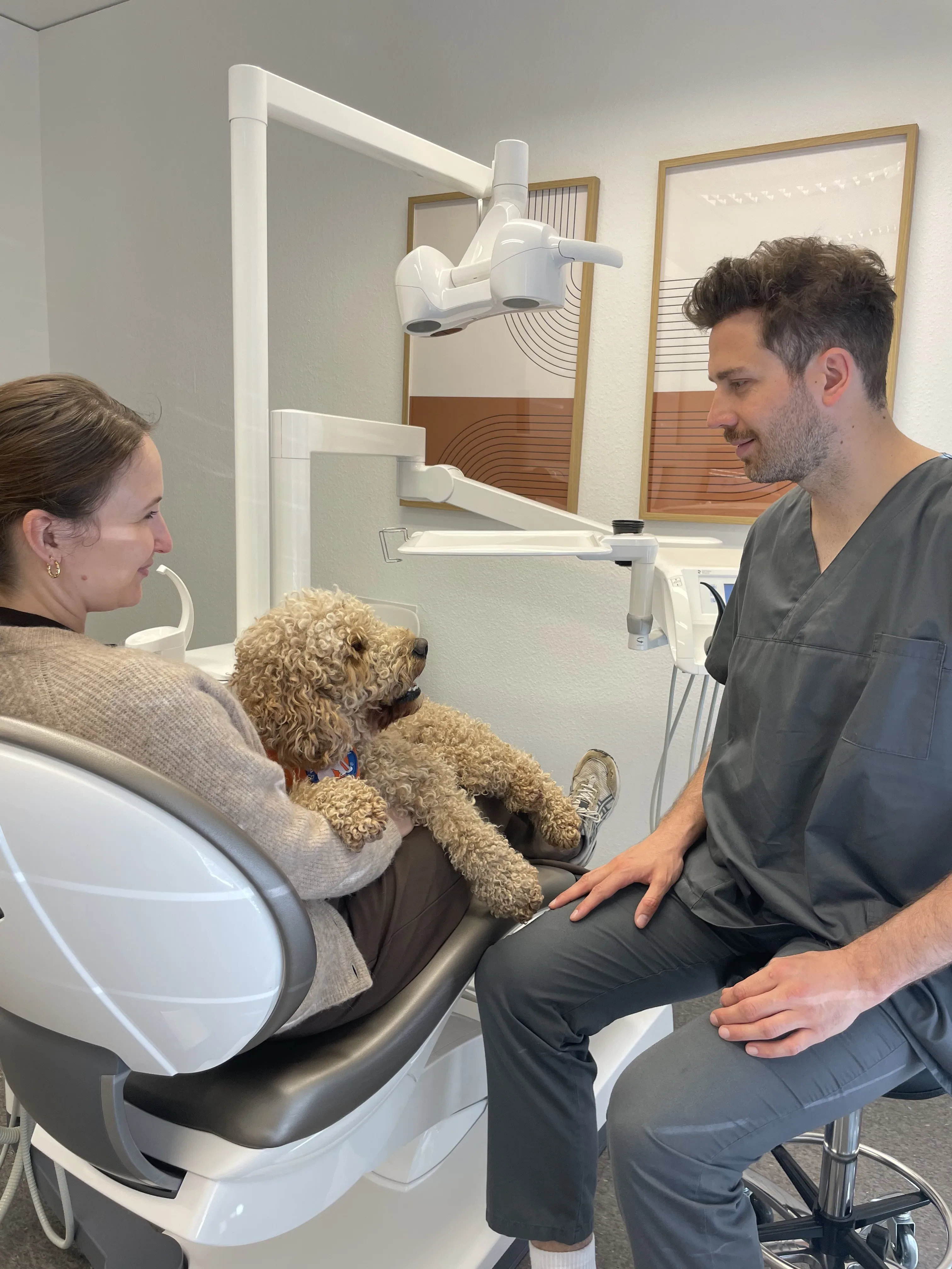 Patientin streichelt Therapiehund Oskar im Behandlungsstuhl während des Vorgesprächs mit dem Zahnarzt